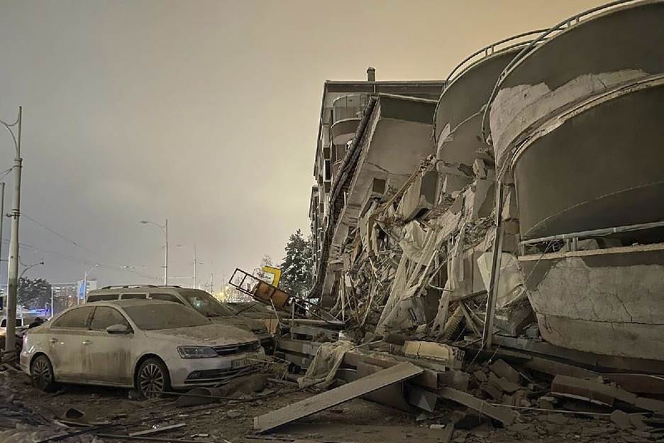 Damaged vehicles sit parked in front of a collapsed building