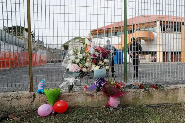 PHOTO: Members of the Guardia di Finanza stand next to floral tributes laid at the fence of PalaMilone sports hall, where victims of a deadly migrant shipwreck are being held, in Crotone, Italy, Feb. 27, 2023. (Remo Casilli/Reuters)