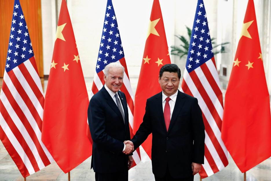 Two men shaking hands in front of flags  Description automatically generated