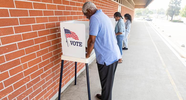 A person putting his vote into a ballot box  Description automatically generated