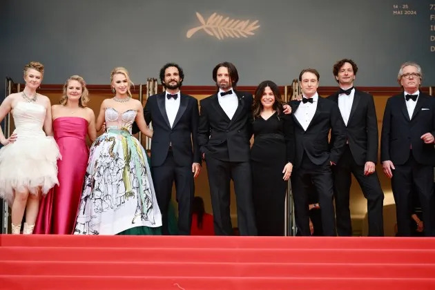 A group of people standing on a red carpet  Description automatically generated