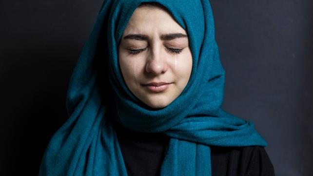 A person wearing a blue scarf crying  Description automatically generated