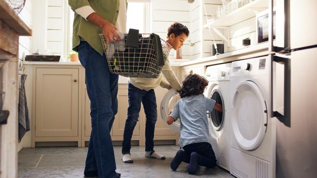 A person and two children looking at a washing machine  Description automatically generated