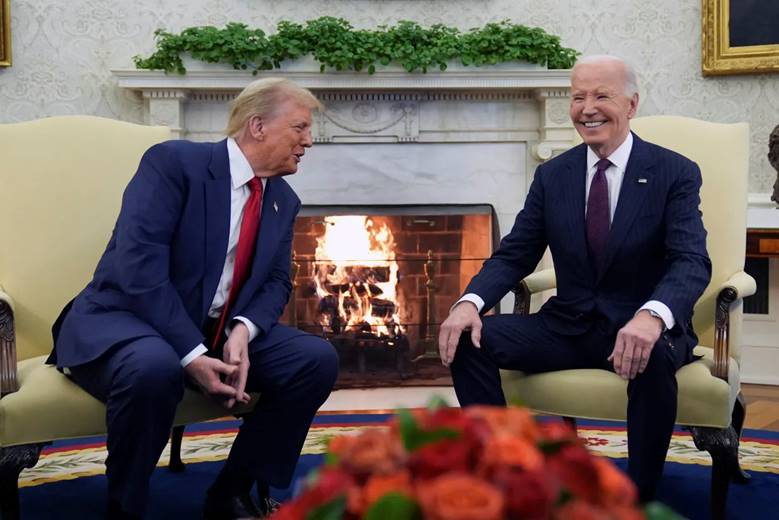 Two men in suits sitting in front of a fireplace  Description automatically generated