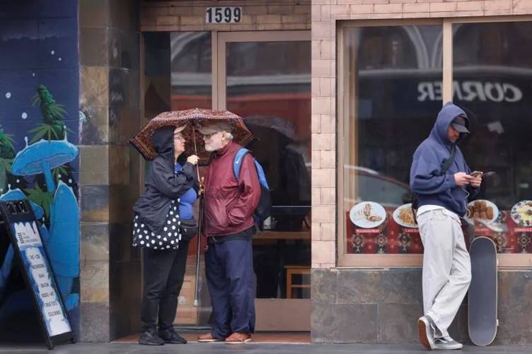 People share an umbrella as they stand on Haight Street, Wednesday, Nov. 13, 2024, in San Francisco. (Lea Suzuki/San Francisco Chronicle via AP)