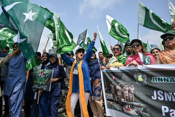 People at a street demonstration, many waving flags and others holding signs.