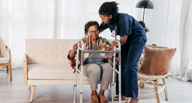 A nurse helping a person to walk on a walker  Description automatically generated