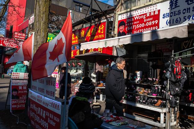 Visitors at an outdoor shop beneath business signs and with two Canadian flags posted 