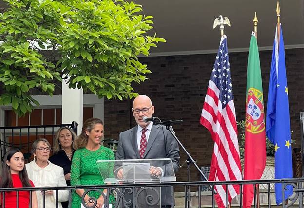 A person standing at a podium with a microphone and people behind him  Description automatically generated