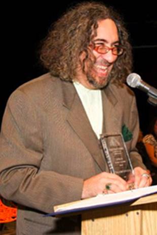 A person with curly hair and a microphone  Description automatically generated