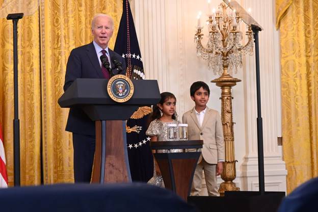 A person standing at a podium with a microphone and a group of people behind him  Description automatically generated