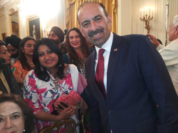 A person in a suit and tie smiling with a group of people in the background  Description automatically generated