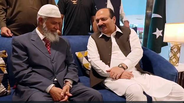 Dr Zakir Naik speaks with an official after arriving in Pakistan on Sept 30. — Radio Pakistan