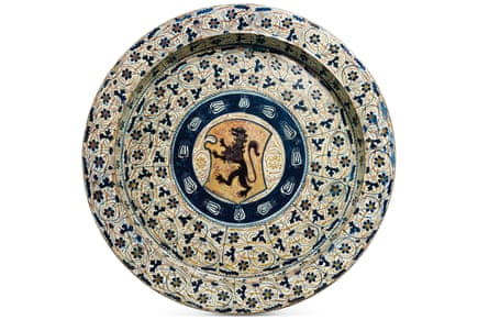 An ornamented dish features a design of blue and yellow flowers encircling a coat of arms