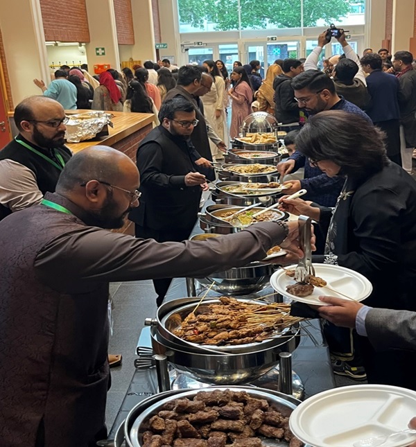 A group of people standing in a line with food in containers  AI-generated content may be incorrect.