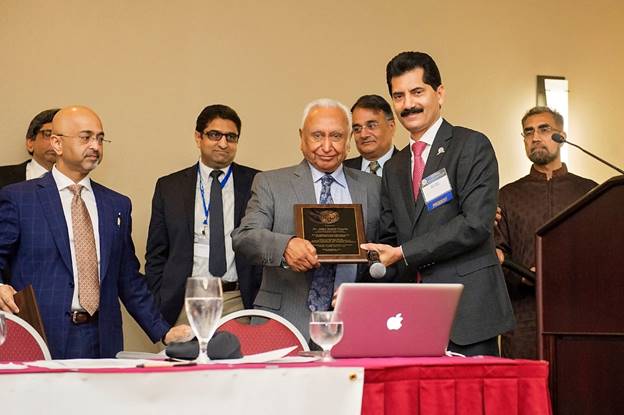 A group of men standing around a table with a person holding a plaque  Description automatically generated