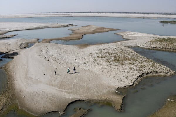 A view from above of three people walking on a patch of land that is surrounded by a wide river.